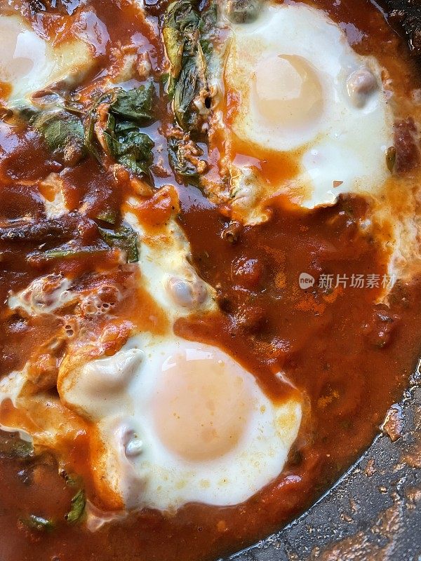 这是地中海健康早餐shakshouka / shakshuka / chakchouka的特写图片，用番茄、辣椒、洋葱、橄榄油和大蒜的酱汁煮熟的鸡蛋，上面放上菠菜和欧芹，俯瞰景色